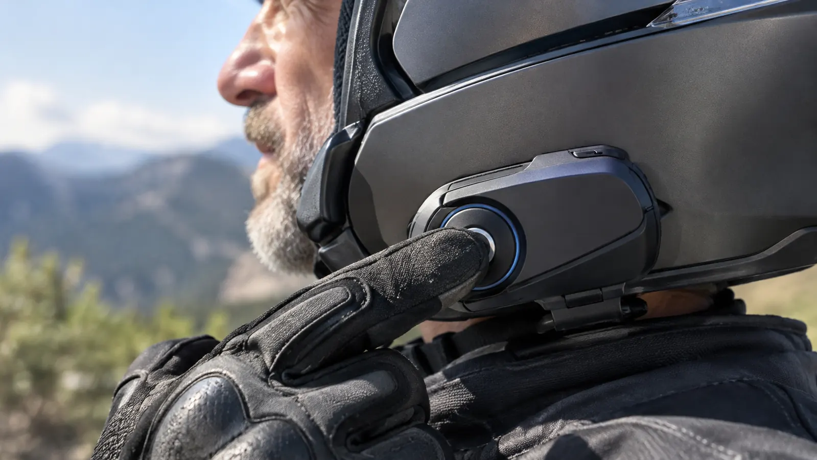 A hand pressing the main button on a helmet intercom mounted to the side of a helmet
