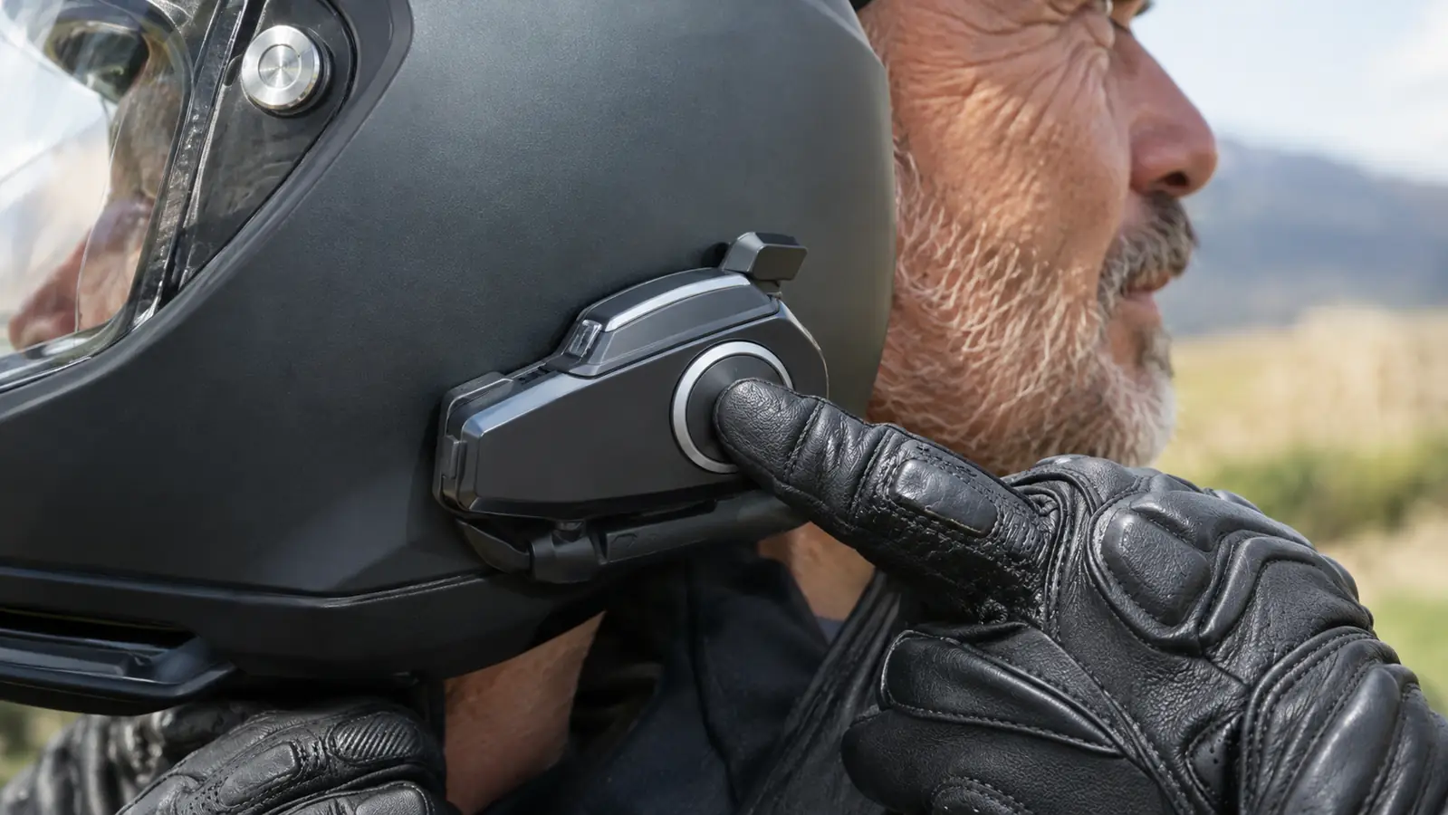 A hand pressing a button on a headset mounted to the side of a motorcycle helmet