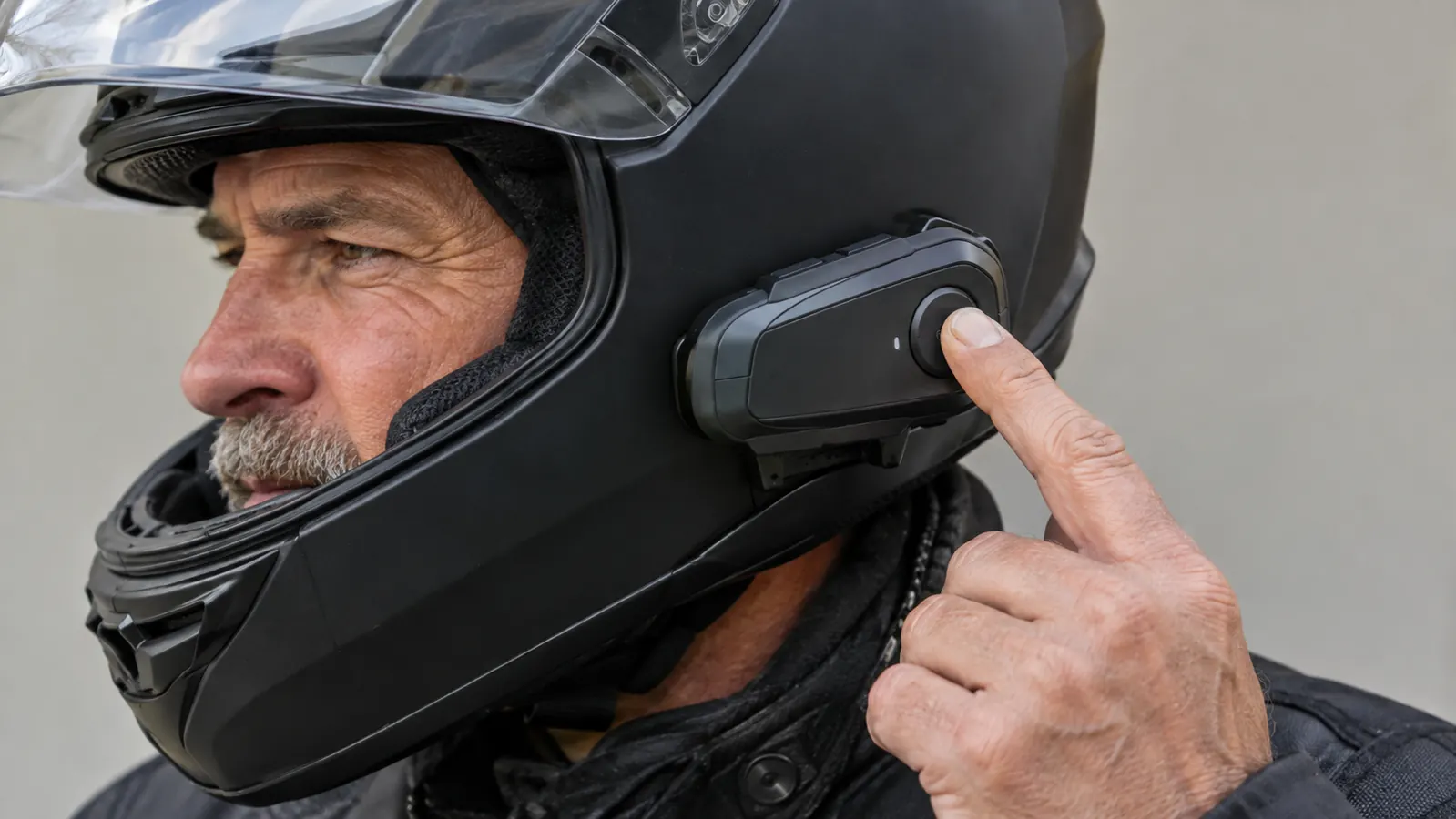 Close view of a hand pressing a small round button on a headset unit mounted to the side of a helmet