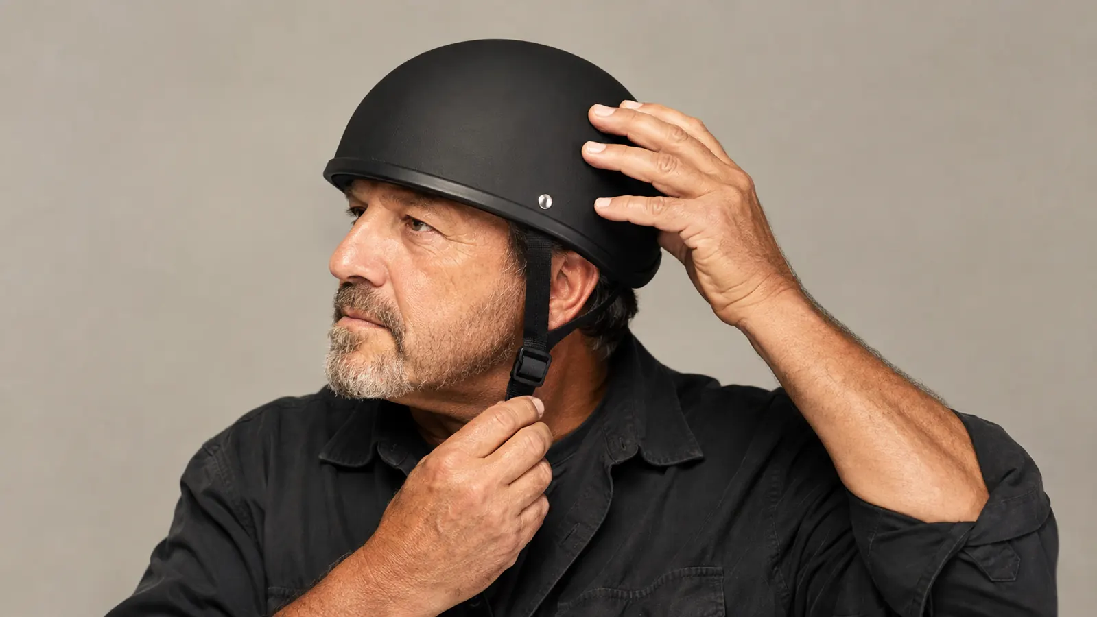 A rider adjusting a half helmet strap with one hand while holding the helmet steady with the other