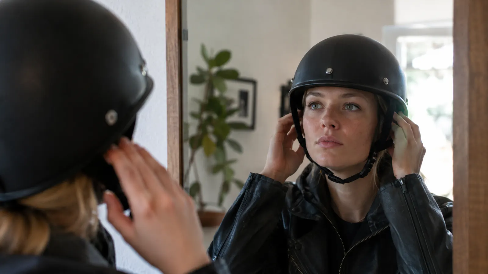A rider checking the fit of a half helmet in a mirror, with the helmet sitting level on the head