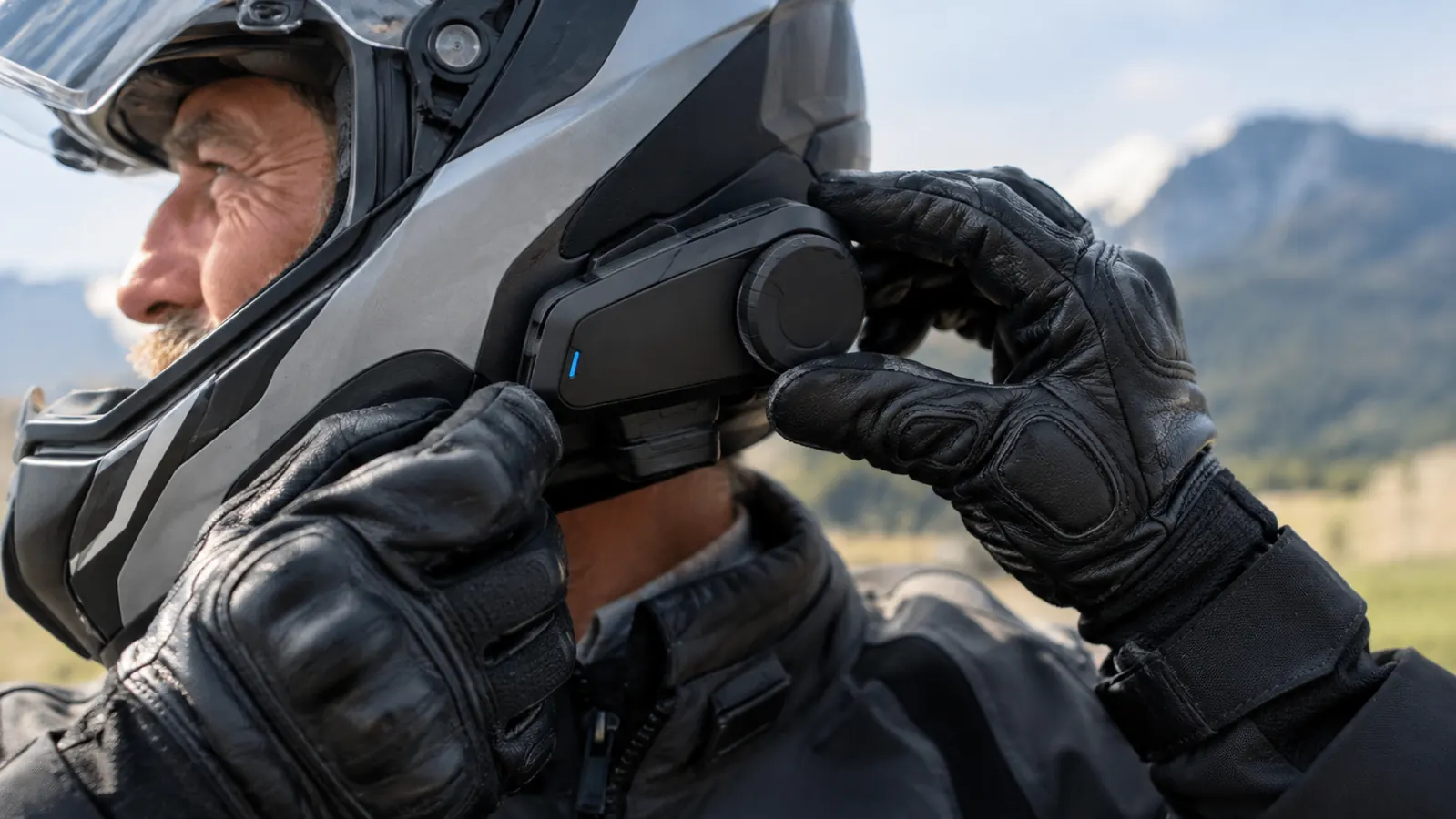 A close view of a rider's gloved hand adjusting the unit on the side of a helmet before a ride